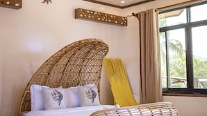 Une pièce comprenant un lit, un ventilateur de plafond, une fenêtre et un banc en osier.