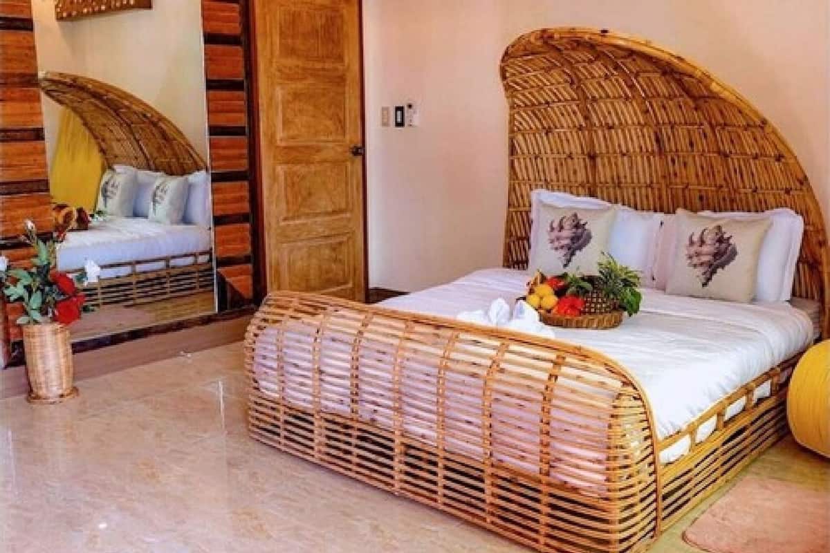 Une chambre avec un lit en osier, un miroir et une plante en pot.