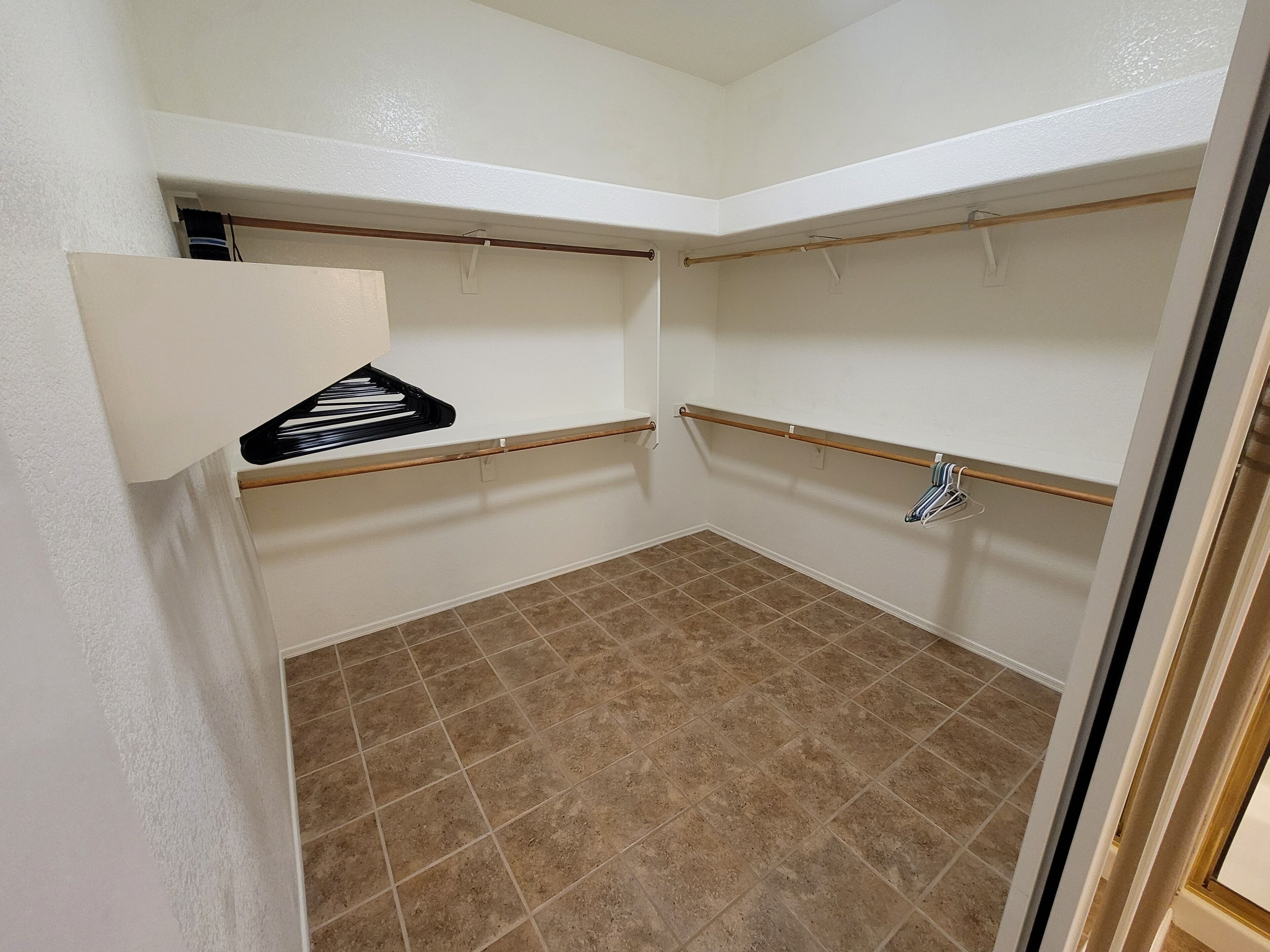 A small, empty room with beige tiled flooring, white walls, and two wooden shelves.