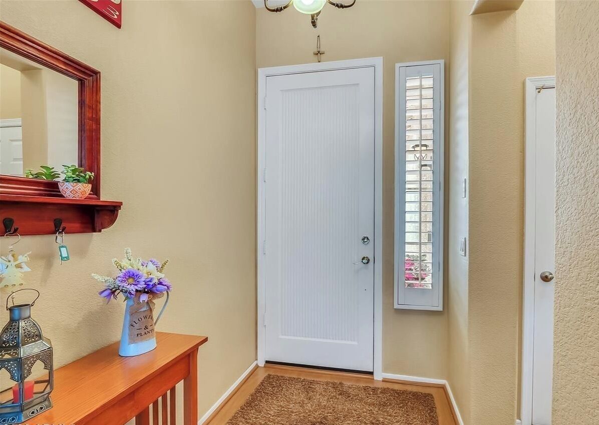 A hallway with a wooden console table, a vase with flowers, a door, and a wall-mounted light fixture.