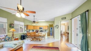 A spacious living room with a large sofa, a coffee table, and a dining area with chairs and a table. There is a kitchen area with cabinets and appliances in the background. - Spacious 4 bed, Sparkling Pool, Game Room, Pool Table, Arcade, Sleeps 19 (Mesa)