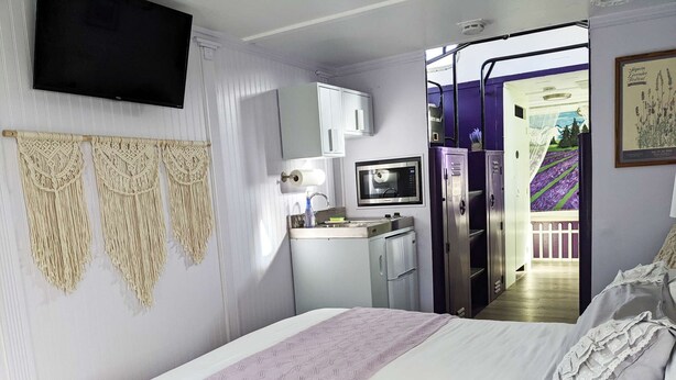 A bedroom with a bed, a TV, a kitchenette, and a view of a garden. - Lavender Limited at Olympic Railway Inn - Pet Friendly (Sequim)