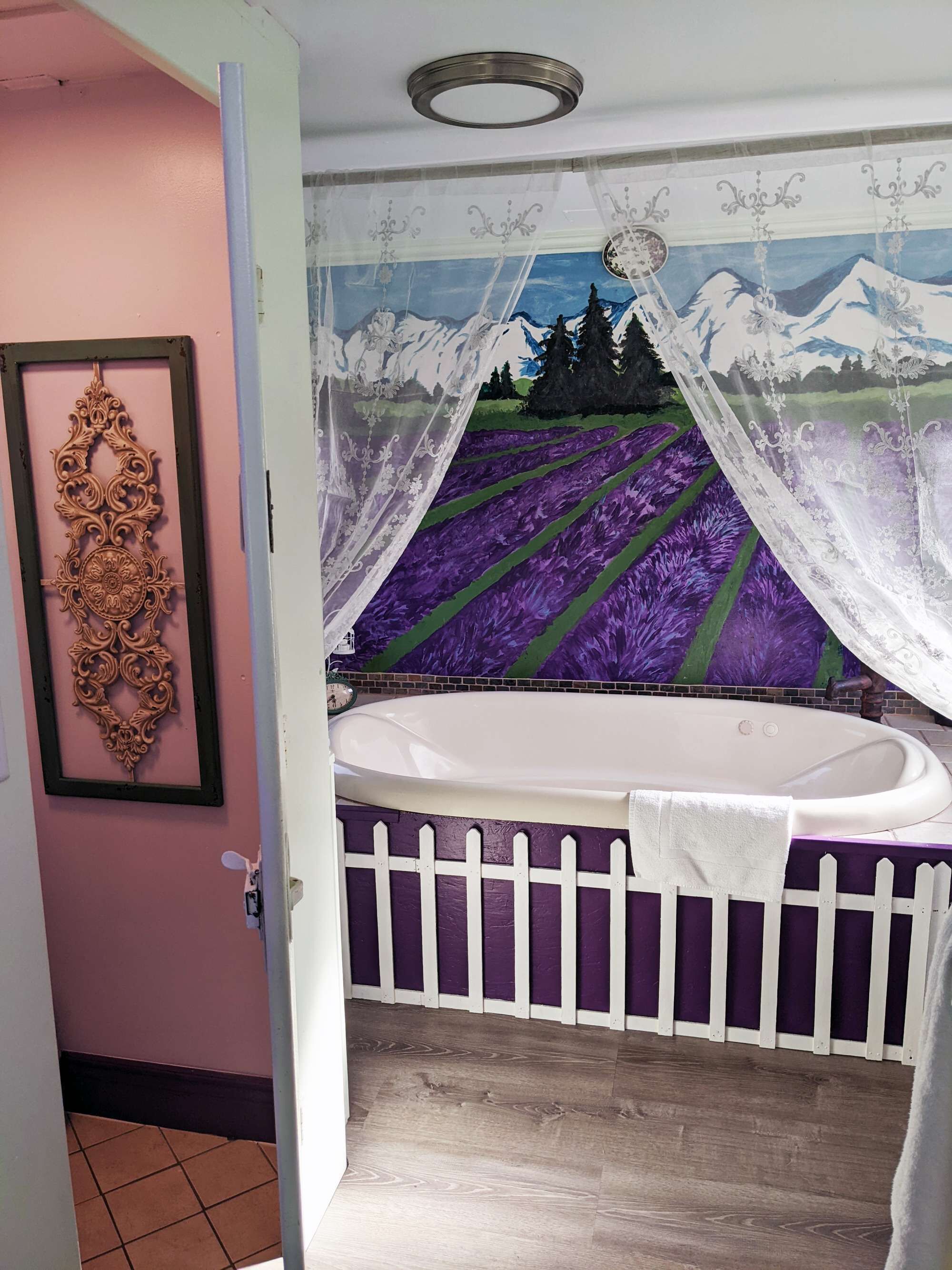 A bathroom with a purple and white color scheme, a decorative wall piece, a white bathtub, and a shower curtain.