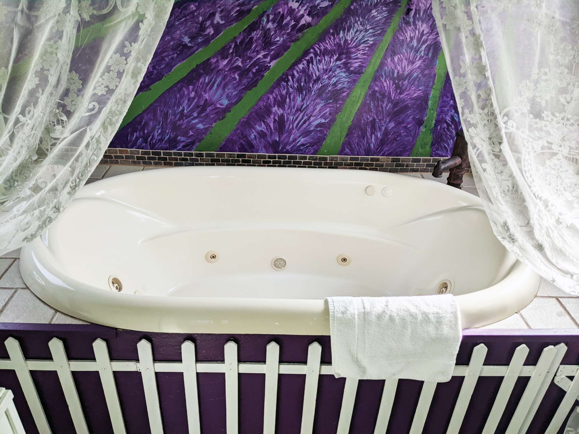 A bathtub with a white interior, a white towel, and a purple floral wall.