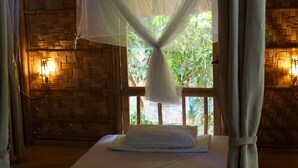 A bed with a mosquito net, wooden walls, and a window with a view of greenery.