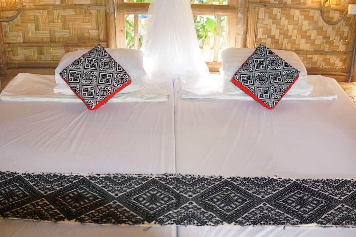 A bed with white linens and two decorative pillows with geometric patterns.