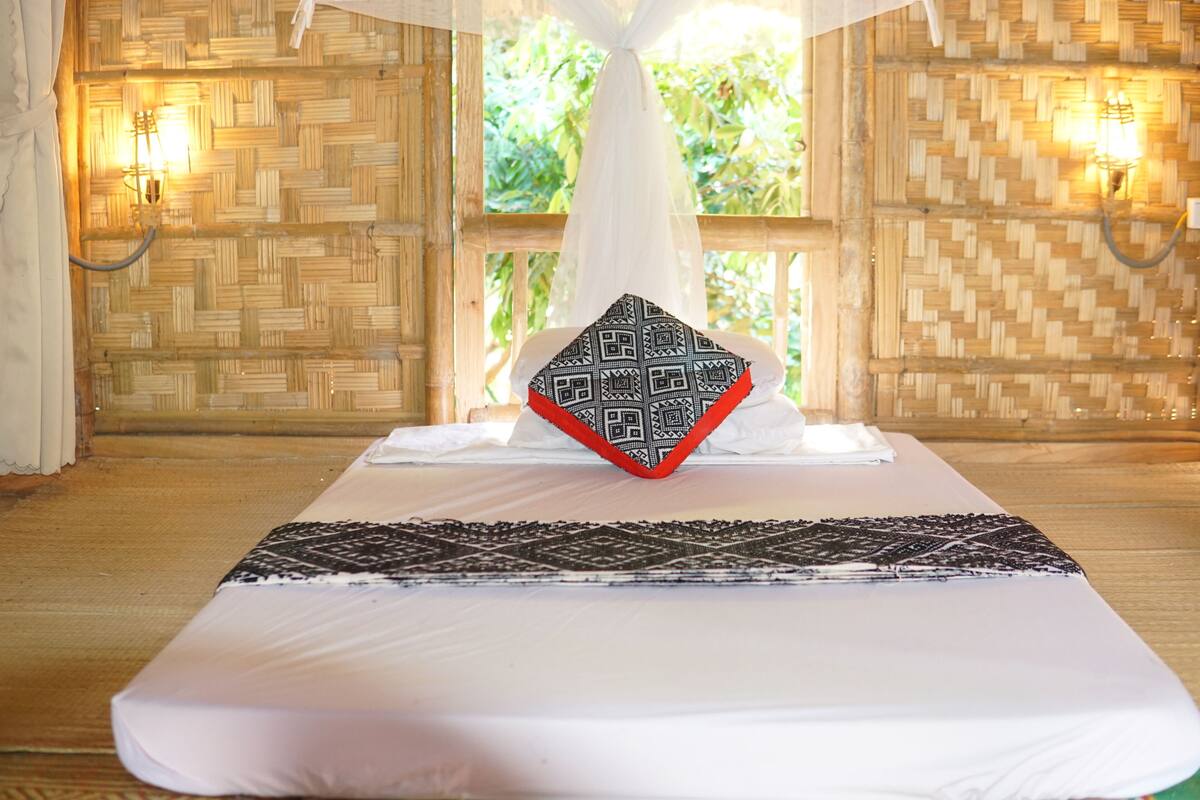 A room with a bed, a decorative pillow, and a woven wall.