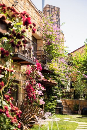 En bygning i sten med balkon, omgivet af frodig vegetation og blomstrende planter.