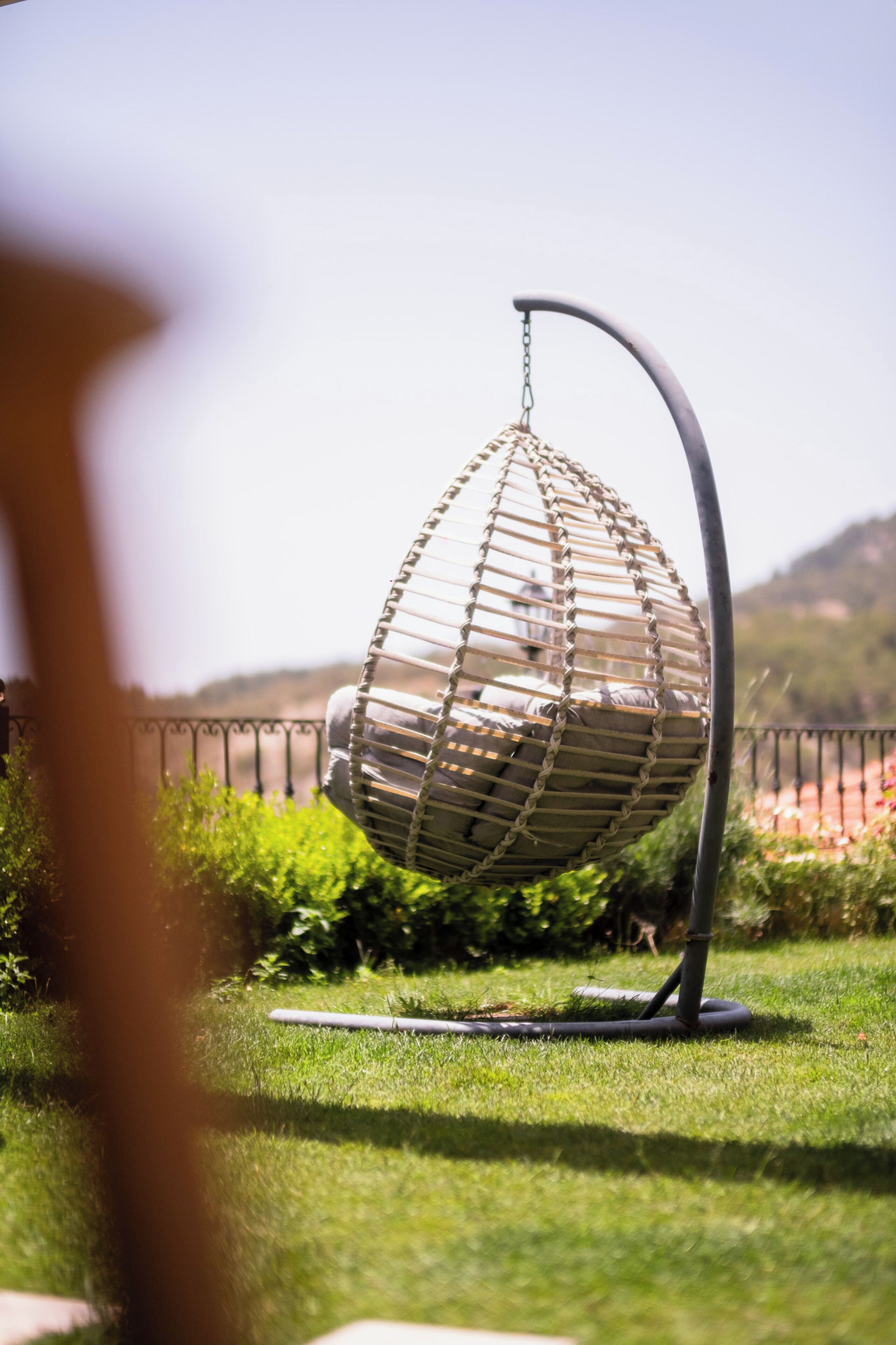 A hanging chair in a garden with a metal stand and chain.
