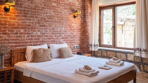 A room with a brick wall, a large bed with white linens, a hanging light fixture, and a window with curtains. - Arıklı Han Kazdağları (Ayvacik)