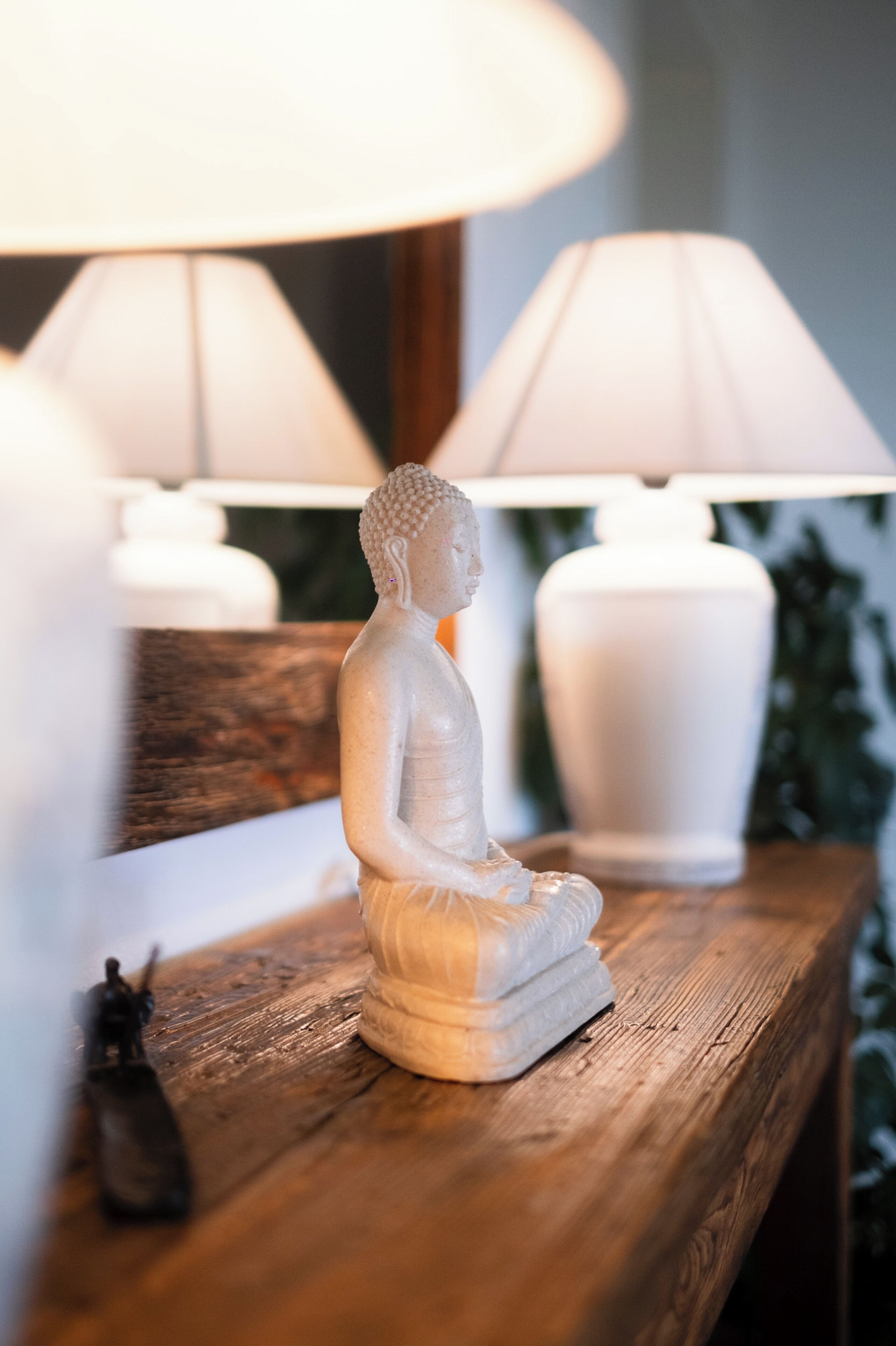 Una estatua de una figura sentada sobre una superficie de madera, con dos lámparas al fondo.