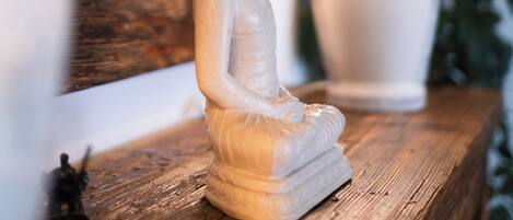 A statue of a seated figure on a wooden surface, with two lamps in the background.