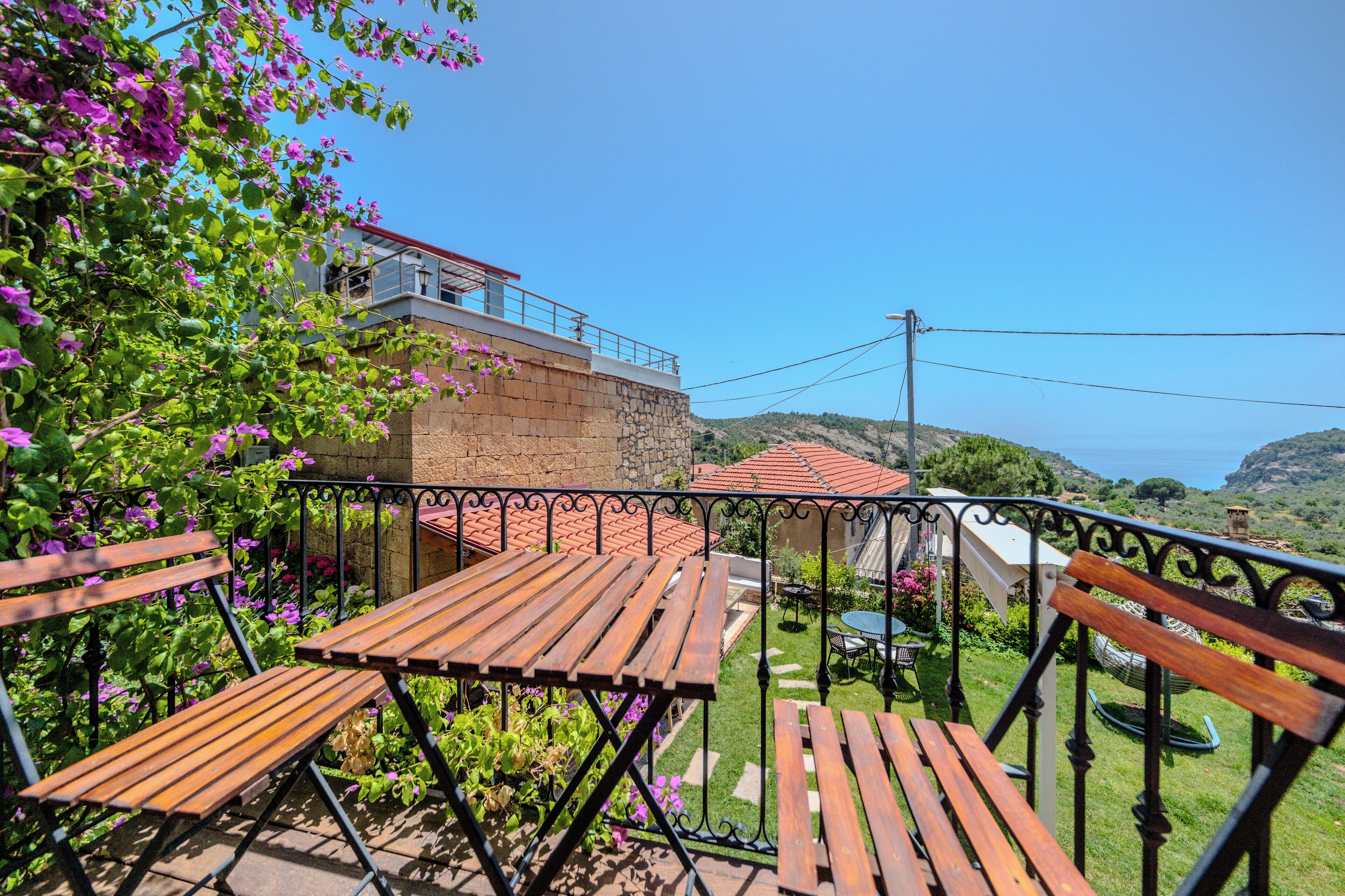 Un patio con bancos y mesas de madera, un muro de piedra y vista al mar.