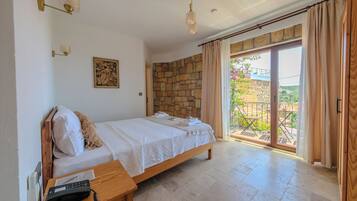 Un dormitorio con cama, mesita de noche de madera, teléfono, pared de piedra y vistas al exterior a través de una puerta de cristal.