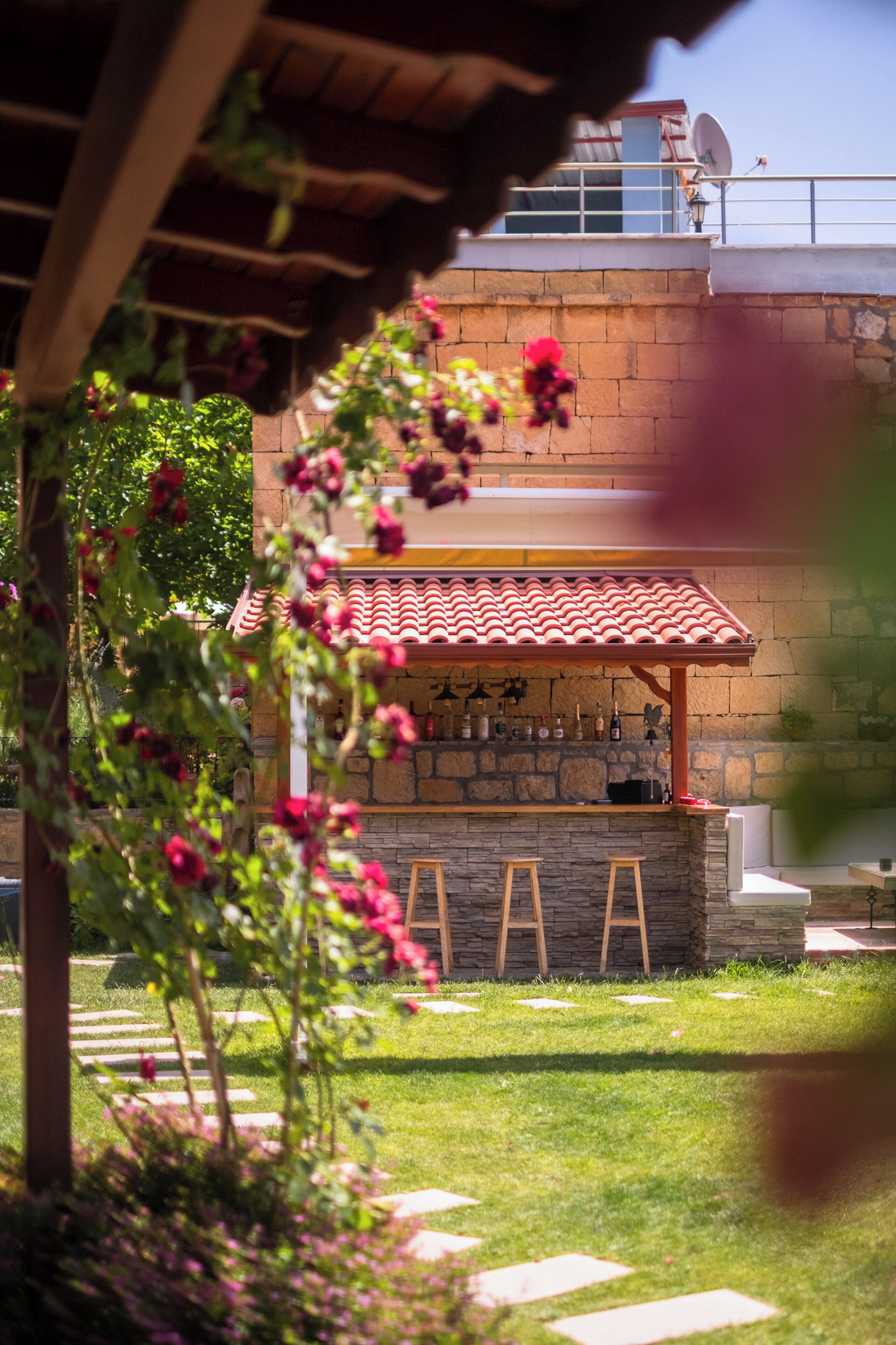 A stone bar area with a tiled roof, surrounded by greenery and a stone wall.