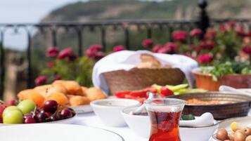 Una mesa servida con comida y bebidas, vista al mar y flores de fondo.