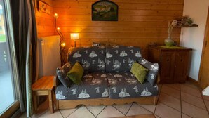 Een gezellige woonkamer met een houten vloer, een bank met een motief uit de natuur, een kleine tafel en een aan de muur hangend schilderij.