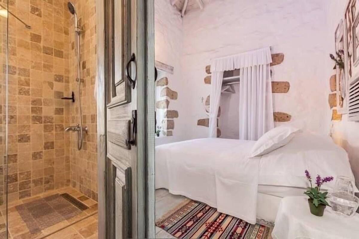 Une chambre à coucher avec un lit, une table de chevet ornée d’une plante et un espace douche avec un mur carrelé.