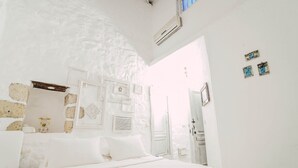 Een slaapkamer met witte wanden, een bed, een stoel en een deur naar een andere kamer.