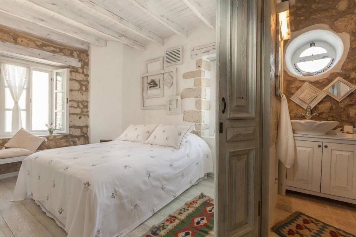 Une chambre à coucher avec un lit, une fenêtre, un mur en pierre et une salle de bain avec un lavabo et un miroir.