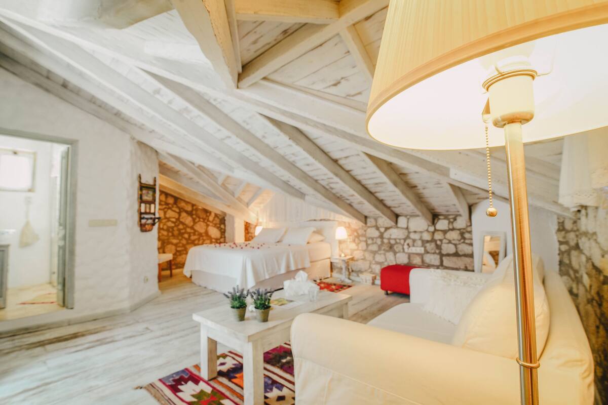 Une pièce chaleureuse et bien éclairée, avec un lit, un canapé, une table avec une lampe et un mur en pierre.