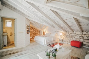 Ein Schlafzimmer mit einer Steinsäule, einem Bett, einem roten Hocker und einem weißen Tisch mit Pflanzen.