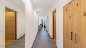 A hallway with wooden doors, a kitchen area in the distance, and a view of the outdoors.