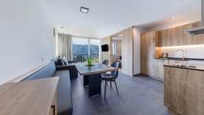A modern kitchen with wooden cabinets, a dining area with a table and chairs, and a large window with a view of mountains.