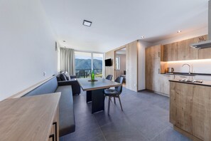 A modern kitchen with wooden cabinets, a dining area with a table and chairs, and a large window with a view of mountains.