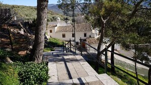 A stone staircase leading to a building with a tiled roof, surrounded by trees and a view of a hillside.
