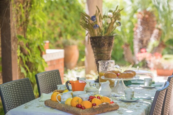 Un espace de restauration en plein air avec une table dressée pour le petit-déjeuner, comprenant des fruits, des viennoiseries et un coin café.