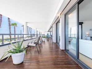 Varanda ampla com piso de madeira, vasos de plantas e área de estar.