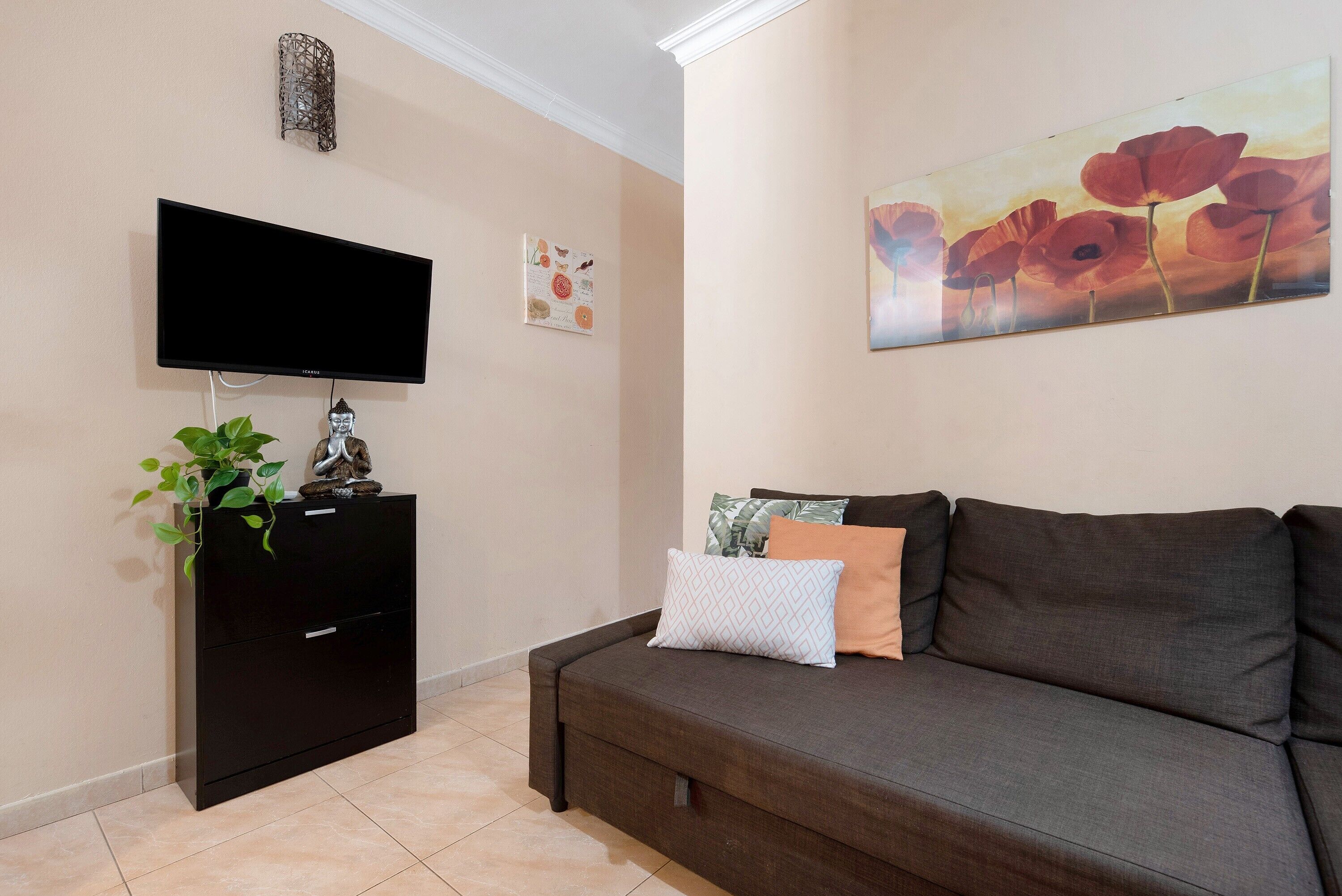 Ein Wohnzimmer mit einem Flachbildfernseher, einem schwarzen Schrank, einer Couch mit Kissen, einem Gemälde von Mohnblumen und einem kleinen Wanddekor.