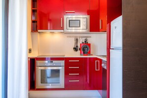 Une cuisine de taille réduite avec des meubles rouges, un four à micro-ondes, un four traditionnel et un réfrigérateur.