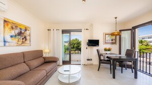 Un salon moderne comprenant un canapé, une table basse ronde, une table à manger avec des chaises, un téléviseur et un balcon avec vue.