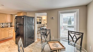 Una cocina moderna con un refrigerador negro, armarios de madera y una mesa de comedor de vidrio con sillas.