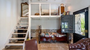 Una habitación con una cama, una silla, una escalera de madera y una puerta con un ventanal.