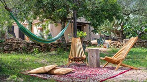 Una hamaca, dos sillas de madera, una manta y una mesa de madera rústica en un jardín.