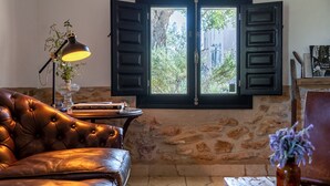 Una habitación con pared de piedra, un sofá de cuero, una mesa con lámpara y una ventana con contraventanas abiertas.