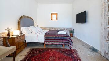 Un dormitorio con cama, mesita de noche, lámpara, televisor y un ventanal.