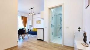 Ein modernes Wohnzimmer mit Sofa, Esstisch und Stühlen. Im Hintergrund ist eine Glasdusche erkennbar.