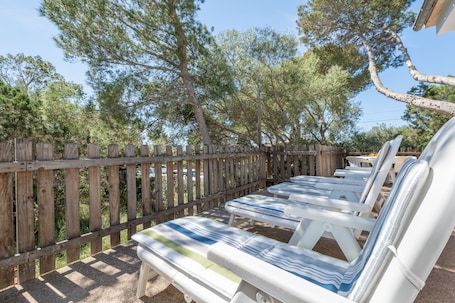 A wooden fence, outdoor lounge chairs, and trees.. Holiday Home 'Es Jaç' with Mountain View and Garden