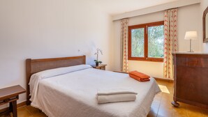 A bedroom with a bed, a nightstand, a lamp, a window with curtains, and a desk.