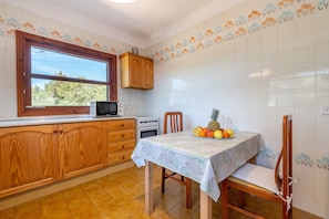 Une cuisine avec des meubles de rangement en bois, une fenêtre, un four à micro-ondes et une table sur laquelle se trouvent des fruits.