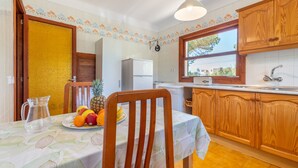 A kitchen with wooden cabinets, a refrigerator, a sink, and a dining table with a fruit plate.
