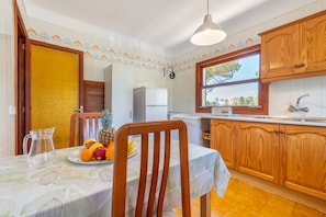 A kitchen with wooden cabinets, a refrigerator, a sink, and a dining table with a fruit plate.