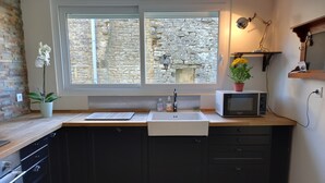 Een moderne keuken met uitzicht op een stenen muur, een inbouwspoelbak, een magnetron en een potplant.