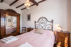 A bedroom with a bed, a wooden dresser, a nightstand, a mirror, and a ceiling light fixture.