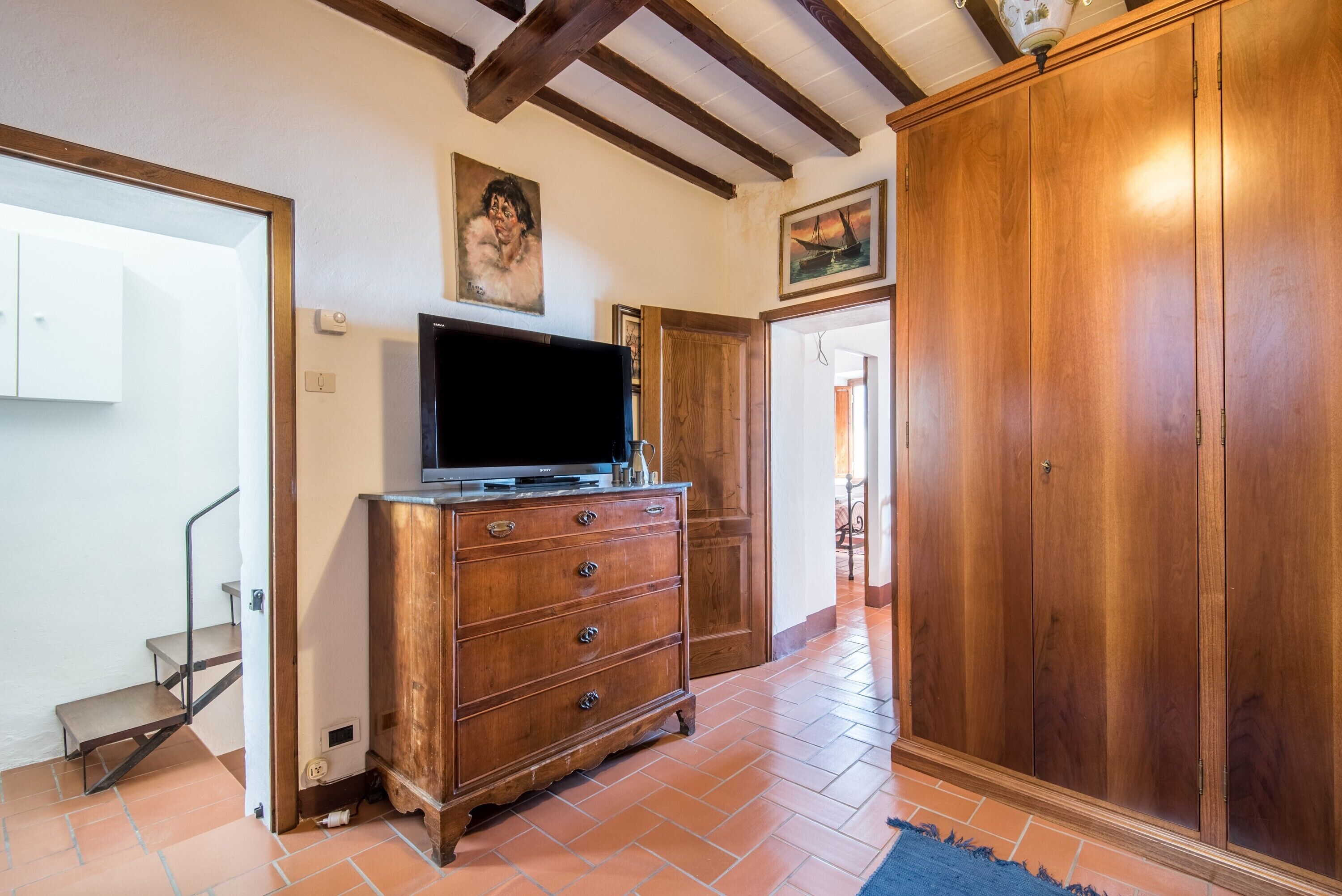 Un couloir avec une armoire en bois, un téléviseur posé sur le dessus, une grande armoire en bois et un escalier.