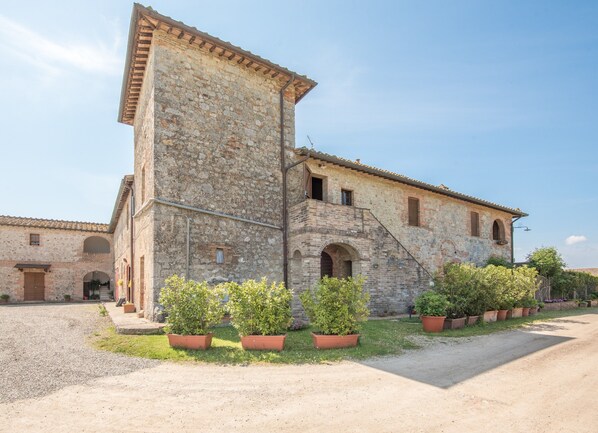 A historic stone building with a central tower, arched windows, and a gravel courtyard.